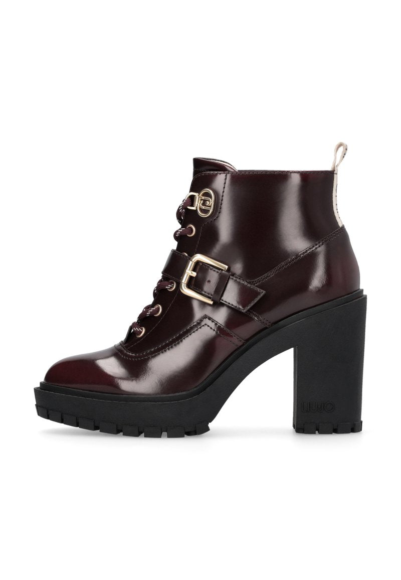 Burgunderfarbene Lackleder-Ankle-Boots mit hohen Absätzen, die Schnür- und Schnallen-Details aufweisen, eine strukturierte schwarze Plateausohle haben und einen kontrastierenden Absatz besitzen.