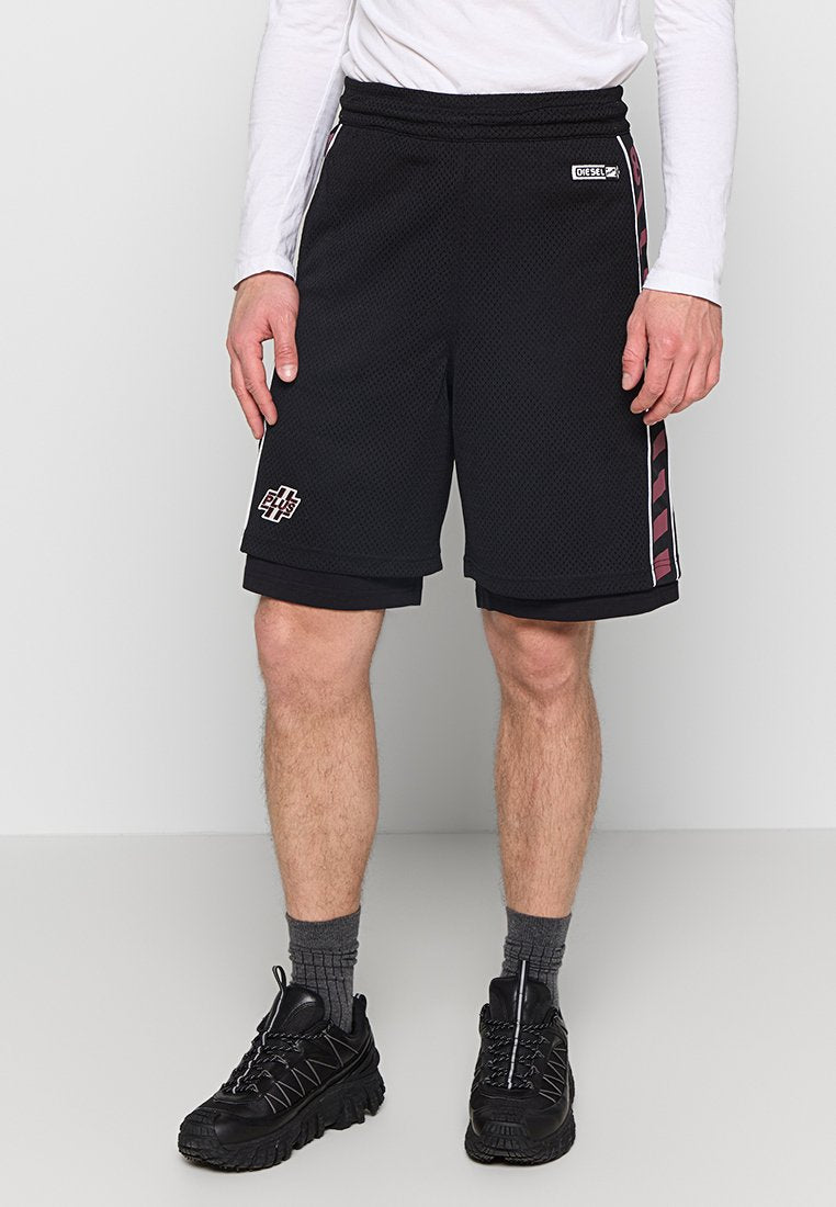 Schwarze Mesh-Shorts mit einem elastischen Bund, seitlichen Streifen in Bordeauxrot und einem Logo-Patch am linken Bein. Getragen mit schwarzen Sneakers und grauen Socken.