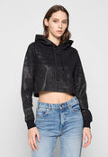 Schwarze, kurz geschnittene Kapuzenjacke mit strukturierter Oberfläche, mit Kapuze und lockerer Passform. Kombiniert mit hoch geschnittenen, hellblauen Jeans.