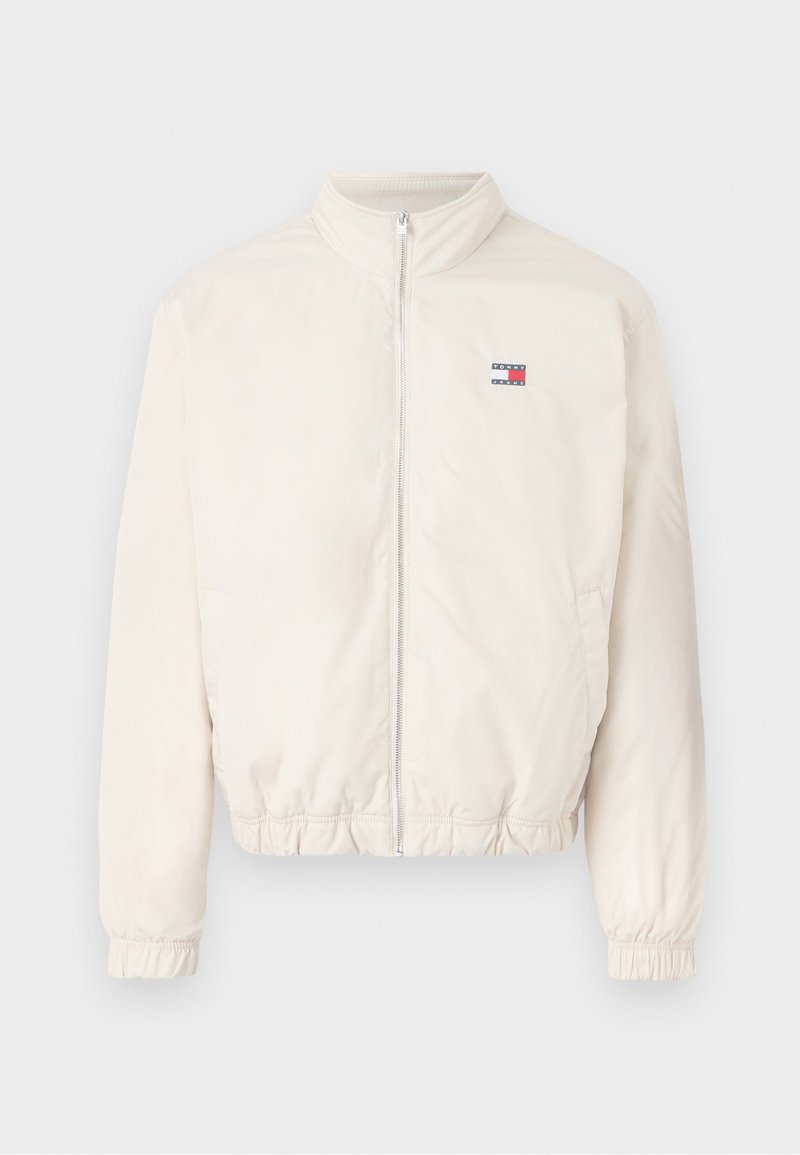 Leichte Bomberjacke aus Creme mit Reißverschluss vorne, elastischen Bündchen und kleinem Logo in Rot und Blau. Glatte Textur, lässiges Design.