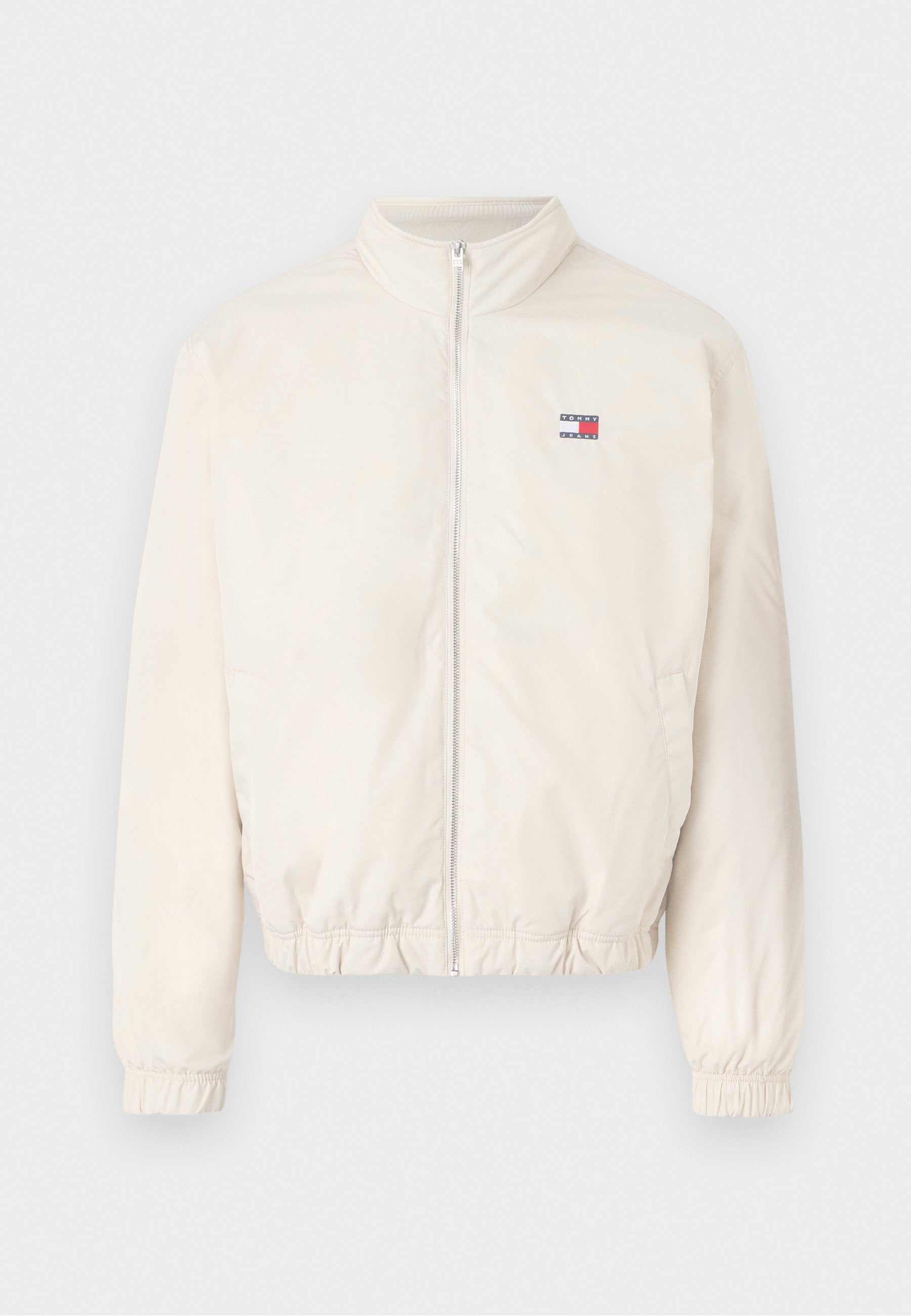 Leichte Bomberjacke aus Creme mit Reißverschluss vorne, elastischen Bündchen und kleinem Logo in Rot und Blau. Glatte Textur, lässiges Design.