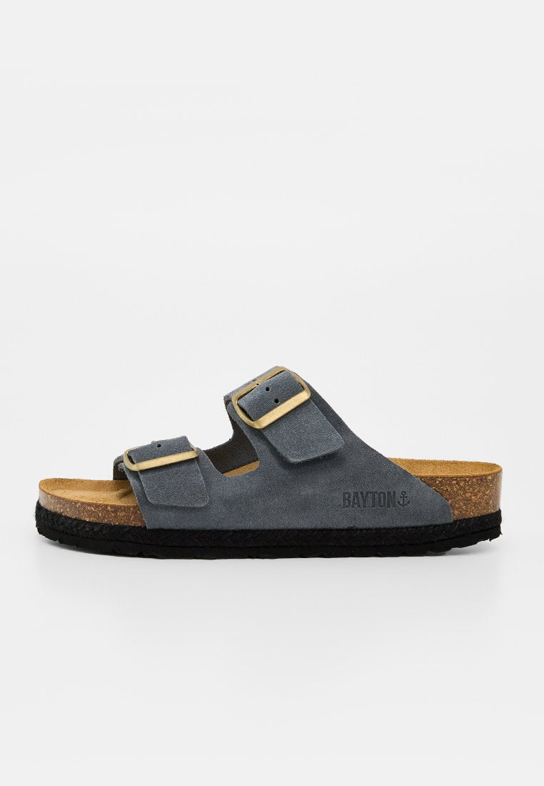 Graue Wildleder-Sandale mit zwei verstellbaren Schnallenriemen, Kork-Fußbett, schwarzer Sohle und Bayton-Logo an der Seite.