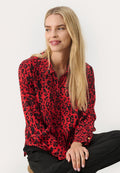 Rote Bluse mit schwarzem Leopardenmuster, langen Ärmeln, Kragen und geknöpften Manschetten. Glatte Textur und lockere Passform. Schwarze Hose rundet das Outfit ab.