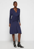 Marineblaue Langarmkleid mit gerafftem Oberteil, V-Ausschnitt, fließendem Rock und kombiniert mit schwarzen, verzierten Knöchelstiefeln. Glatte Stofftextur.