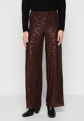 Weite Hosen mit einem schimmernden Pailletten-Design in tiefem Braun. Kombiniert mit einem schwarzen Oberteil und schwarzen Stiefeletten.