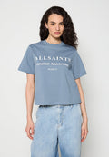 Frau mit lockigem dunklem Haar, die ein blaues AllSaints-Logo-T-Shirt und hellblaue hoch taillierte Jeans vor einem einfarbigen Hintergrund trägt.