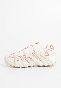 Weißes und beige Sport Schuh mit roten Akzenten, Netzpaneelen und mehreren Riemen über der Oberseite und den Seiten auf weißem Hintergrund.