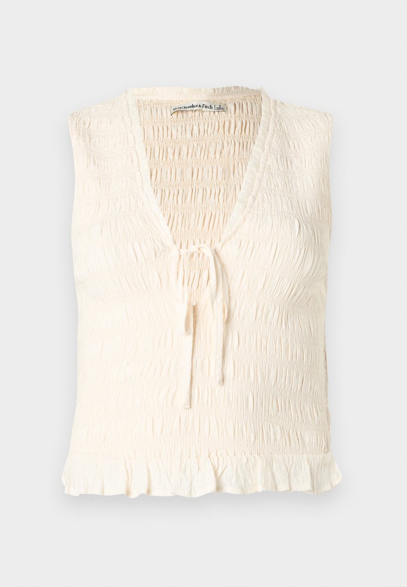 Ärmelloses Oberteil in Creme mit V-Ausschnitt, smockierter Struktur und einer vorderen Knoten-Detail. Ein gerüschter Saum verleiht dem Design Weichheit.