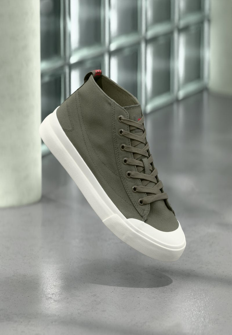 Hohe Sneaker aus olivgrünem Canvas mit braunen Schnürsenkeln, weißer Gummisohle und rotem Akzentdetail an der Rückseite. Glatte Textur und schlichtes Design.