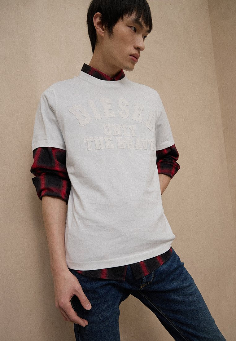 Weißes Baumwoll-T-Shirt mit erhabener "DIESEL ONLY THE BRAVE"-Aufschrift, darüber ein rot-schwarz kariertes Hemd, kombiniert mit blauen Jeans.