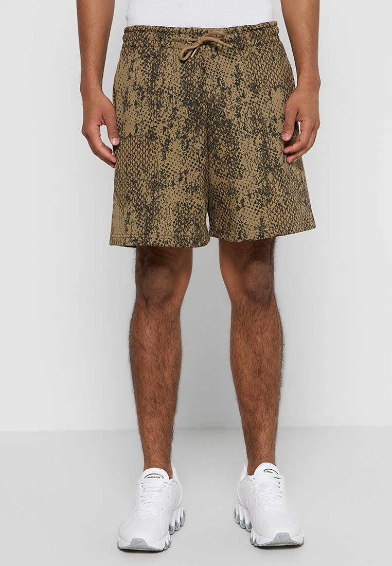 Braune Shorts mit Schlangenhautmuster, elastischem Bund mit Kordelzug und seitlichen Taschen, getragen mit weißen Turnschuhen.