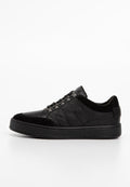 Schwarze Leder-Sneaker mit Wildlederakzenten, Metallösen und einer dicken Gummisohle, von der Seite auf einem weißen Hintergrund gezeigt.