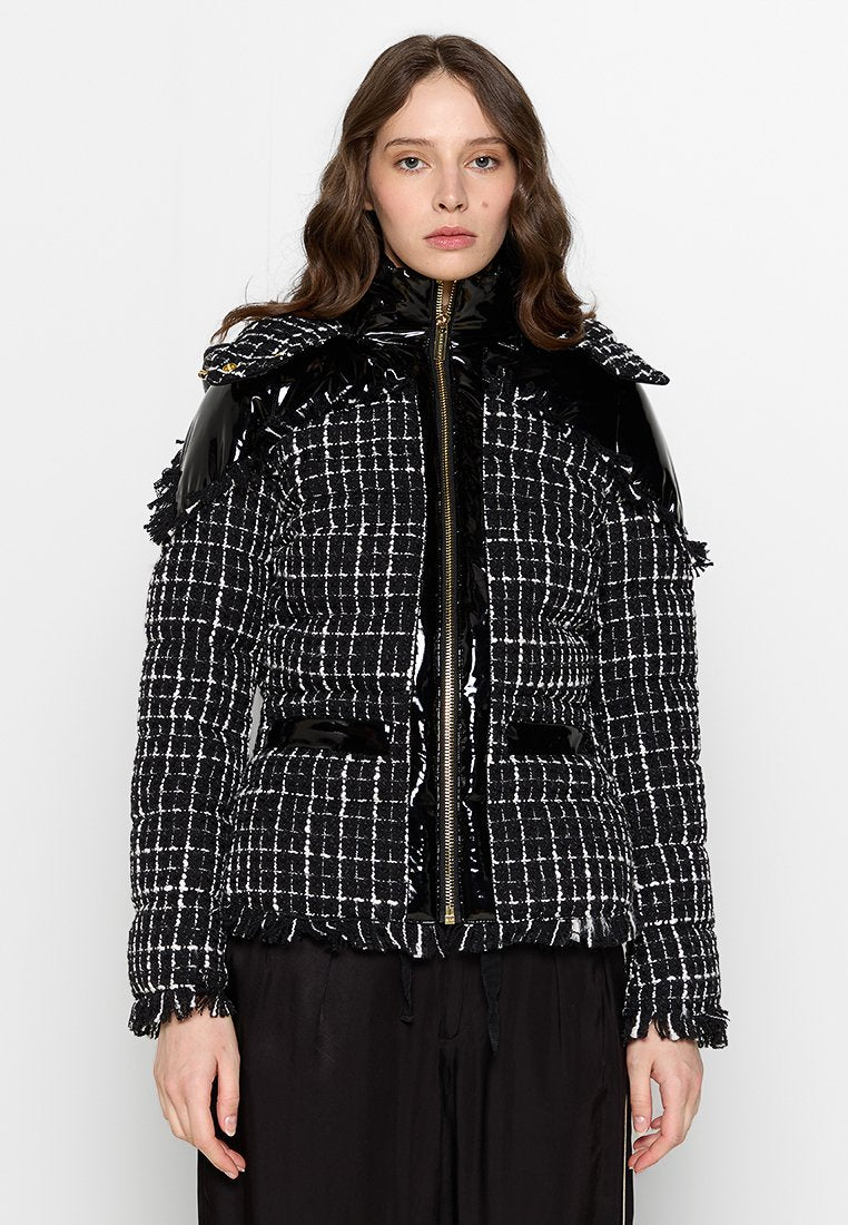 Schwarz-weiß karierte Pufferjacke mit glänzenden schwarzen Lacklederakzenten, Reißverschluss und strukturierten Rüschendetails an den Schultern.