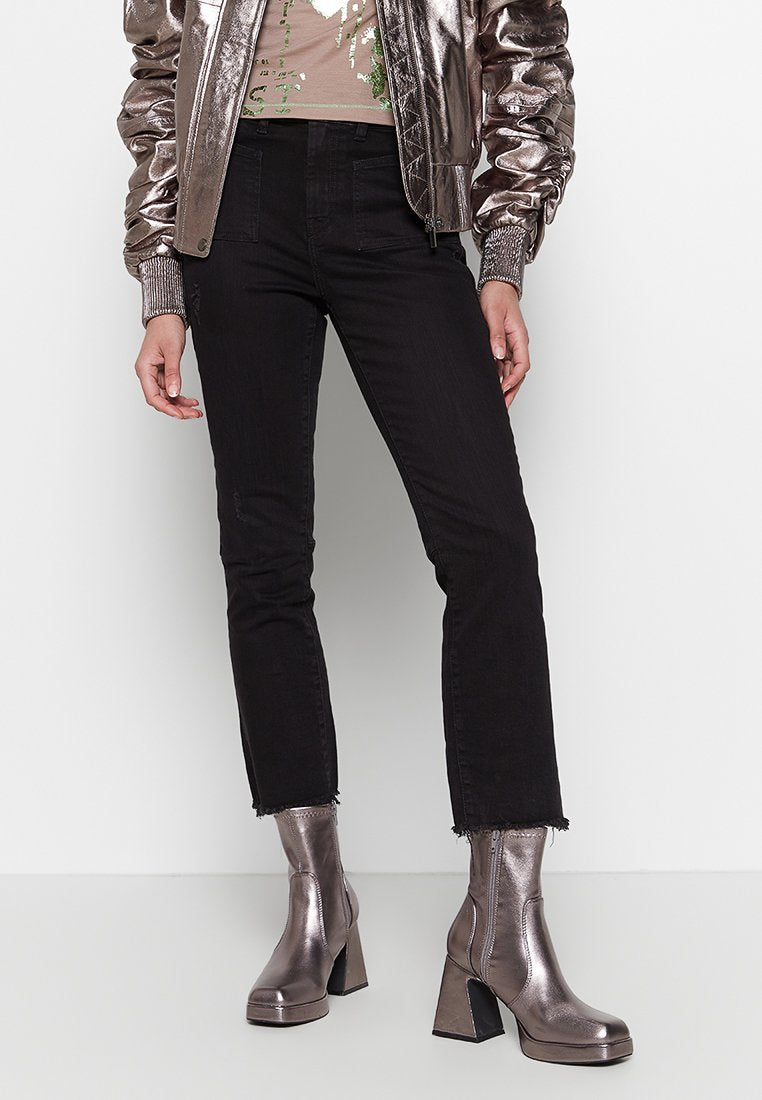 Metallisch glänzende Bomberjacke, beige Oberteil mit grünen Akzenten, schwarze Jeans mit fransigem Saum und glänzende silberne Ankle Boots mit quadratischen Absätzen.