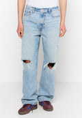 Helle blaue Ripped-Jeans mit fransigen Kanten, geradem Schnitt, fünf Taschen und Metallbeschlägen. Getragen mit dunklen Schuhen mit Streifen.