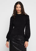 Schwarzer Strickpullover mit hohem Kragen und strukturierten Puffärmeln, kombiniert mit einem schwarzen, mit Pailletten besetzten Rock für den Kontrast.