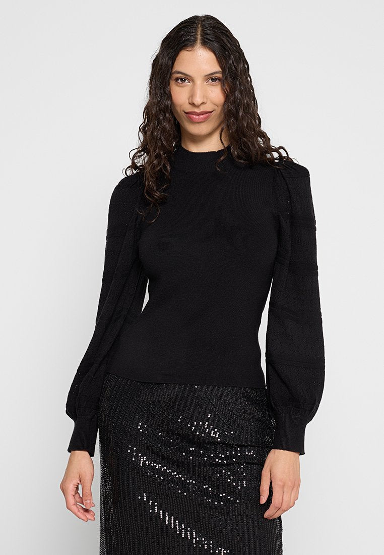 Schwarzer Strickpullover mit hohem Kragen und strukturierten Puffärmeln, kombiniert mit einem schwarzen, mit Pailletten besetzten Rock für den Kontrast.