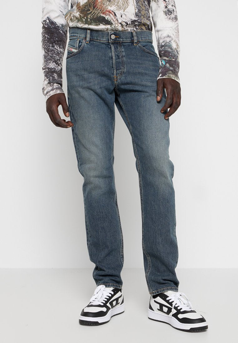 Blaue Denim-Jeans mit normaler Passform, ausgestattet mit einem klassischen Fünf-Taschen-Design und kontrastierenden Nähten. Getragen mit schwarz-weißen Sneakern.