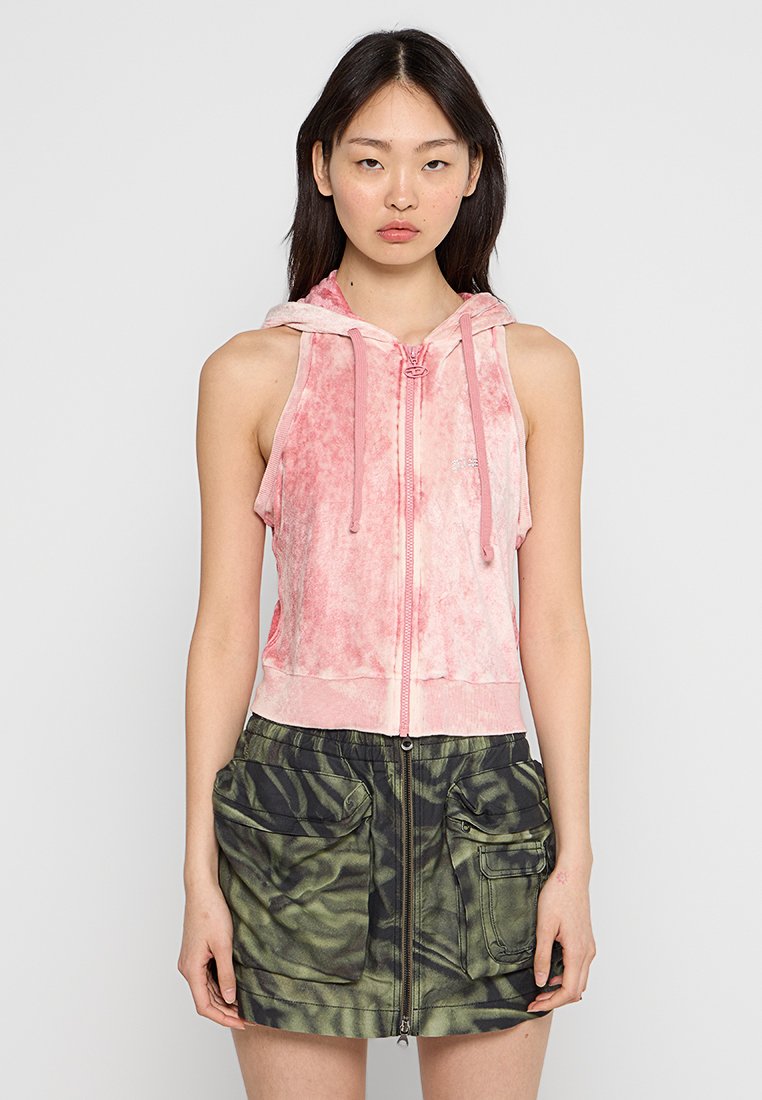 Rosa Zip-up Kapuzenjacke aus weichem, strukturiertem Stoff mit Kordelzug, kombiniert mit einem grünen Camouflage-musternden Rock mit großen Taschen.