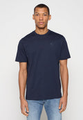 Navyblaues Baumwoll-T-Shirt mit Rundhalsausschnitt und kurzen Ärmeln, versehen mit einem dezenten, aufgedruckten Logo auf der Brust. Kombiniert mit hellblauen Jeans.