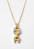 Goldene Halskette mit einem Anhänger, der zwei Hufeisenformen zeigt, von denen eine mit kleinen klaren Kristallen verziert und mit "AIGNER." graviert ist