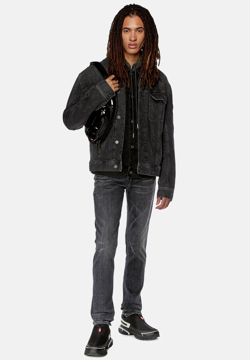 Schwarze Jeansjacke über einem schwarzen Hoodie, graue Jeans und schwarze Schuhe mit weißen Akzenten. Accessories umfassen eine schwarze Tasche. Gerade Passform.