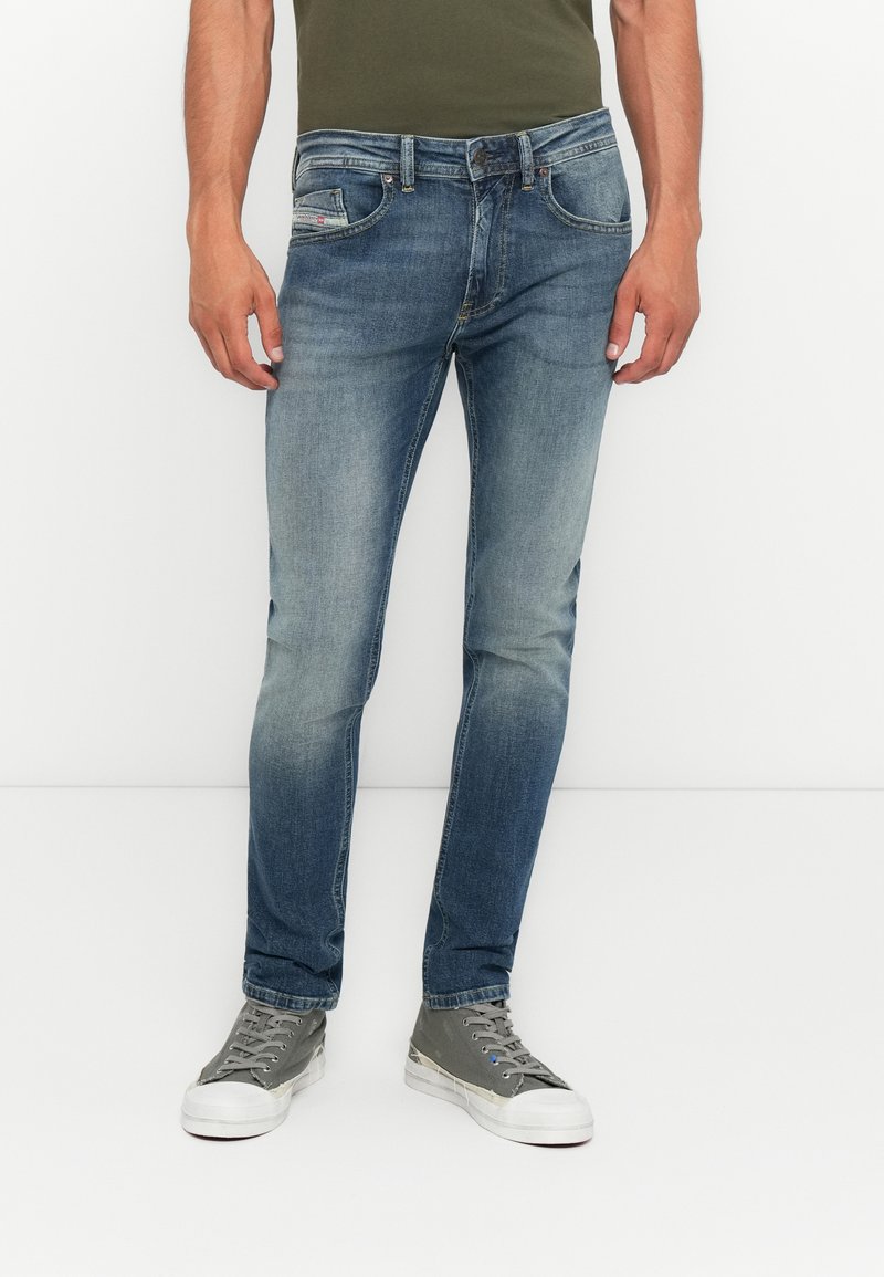 Hellblaue Denim-Jeans mit schmaler Passform, fünf Taschen und kontrastierenden Nähten. Kombiniert mit grauen Sneakers, die eine strukturierte Oberfläche haben.