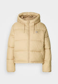 Helle beige Pufferjacke mit einem cropped Design, Reißverschluss vorne und Kapuze. Hat eine gesteppten Textur und ein kleines Logo-Details.