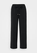 Schwarze, weit geschnittene Hose aus einem weichen Stoff. Verfügt über einen elastischen Bund mit einem Kordelzug und metallischen Enden. Glatte Textur, keine Muster.