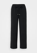 Schwarze, weit geschnittene Hose aus einem weichen Stoff. Verfügt über einen elastischen Bund mit einem Kordelzug und metallischen Enden. Glatte Textur, keine Muster.