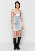 Frau steht in einem enganliegenden grauen und weißen ärmellosen Kleid mit einem roten Logo-Patch und schwarzen kniehohen Stiefeln.