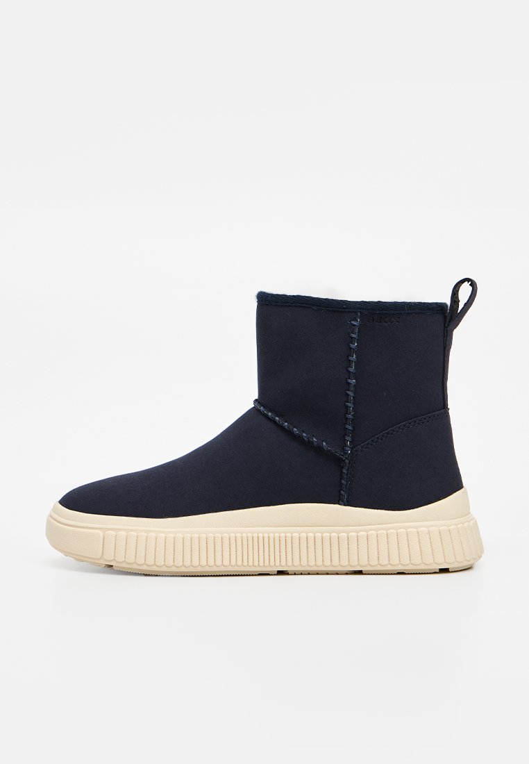 Marineblauer Knöchelstiefel mit elfenbeinfarbener Gummisohle, sichtbaren Nähten und einem Stofflasche zum Ziehen hinten.