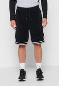 Mann trägt schwarze Basketball-Shorts mit Kordelzug und weißen Streifendetails, weiße Knöchelsocken und schwarze Sportschuhe, steht vor einer weißen Wand.