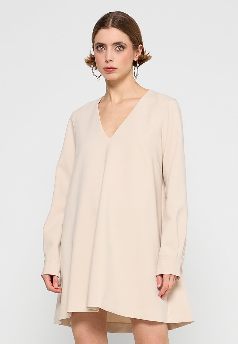 Beiges Kleid mit V-Ausschnitt, langen Ärmeln und einem auslaufenden Saum. Glatte Textur, minimales Design und keine sichtbaren Muster oder Verzierungen.