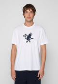 Mann trägt weißes T-Shirt mit schwarzer Grafik eines Affen mit Heiligenschein vorne, steht vor einem einfarbigen hellgrauen Hintergrund.