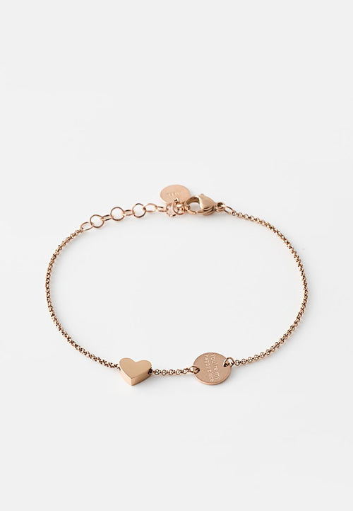 Armband aus Roségold mit einer zarten Kette, die einen herzförmigen Anhänger und einen runden Anhänger mit eingraviertem Text zeigt. Glatte Metalloberfläche.