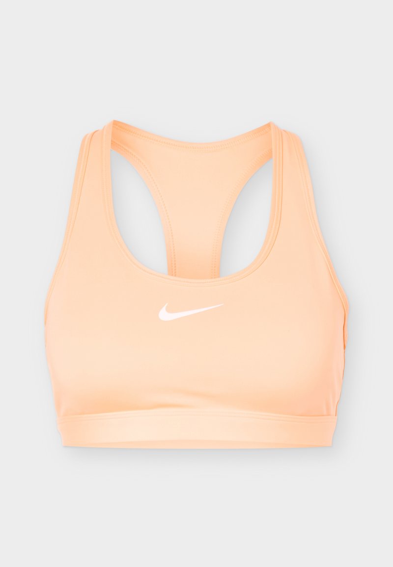 Pfirsichfarbener Nike-Sport-BH mit Racerback-Design und weißem Swoosh-Logo mittig auf der Vorderseite vor hellgrauem Hintergrund.