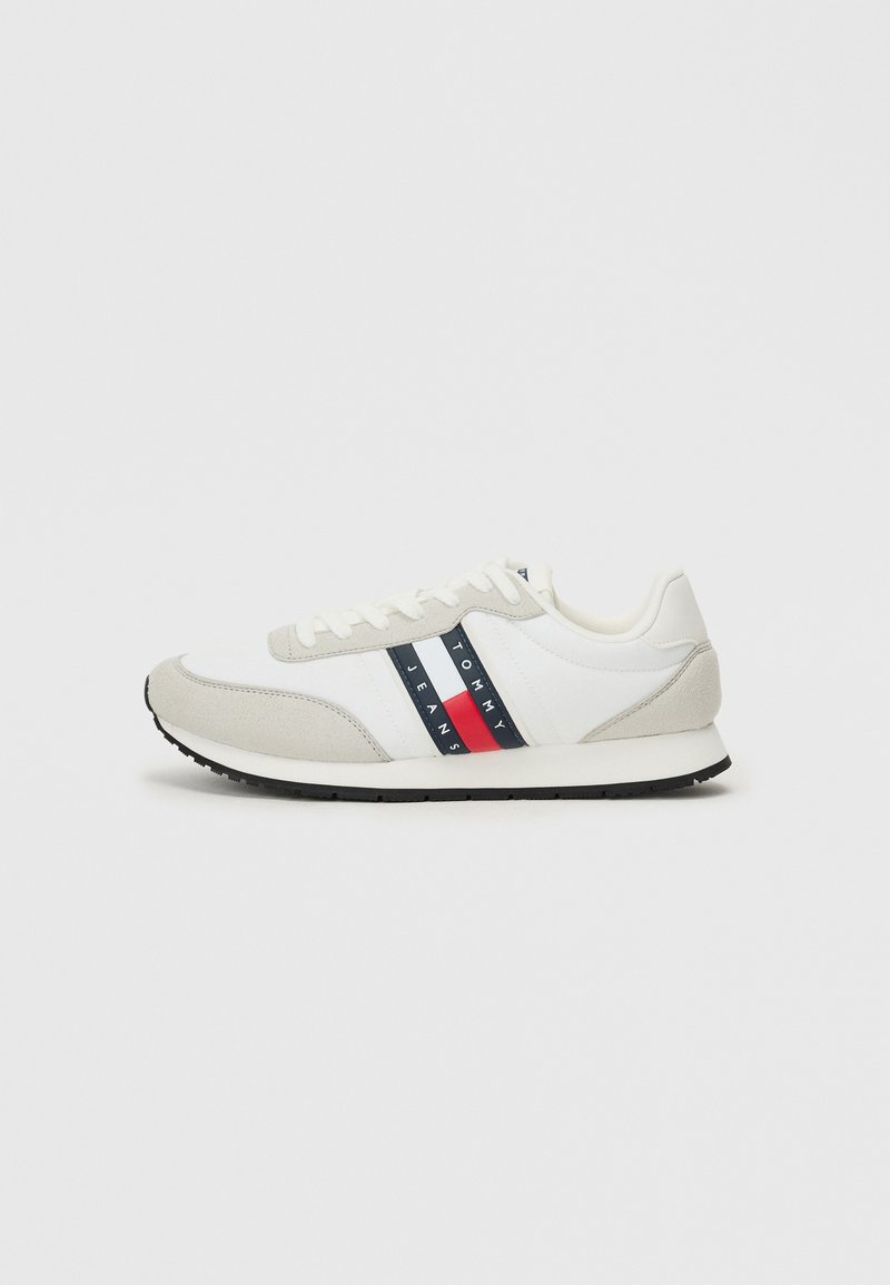 Männliche Laufschuhe mit einem weißen Stoffoberteil, grauen Wildlederakzenten, einer schwarzen Gummisohle und einem rot-blauen gestreiften Logodesign.