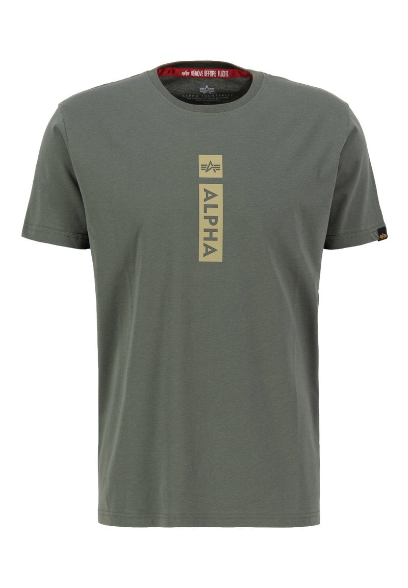 Olivengrünes Kurzarm-T-Shirt aus Baumwolle mit einem zentralen vertikalen goldenen "ALPHA"-Grafik und einem roten "REMOVE BEFORE FLIGHT"-Label im Kragen.