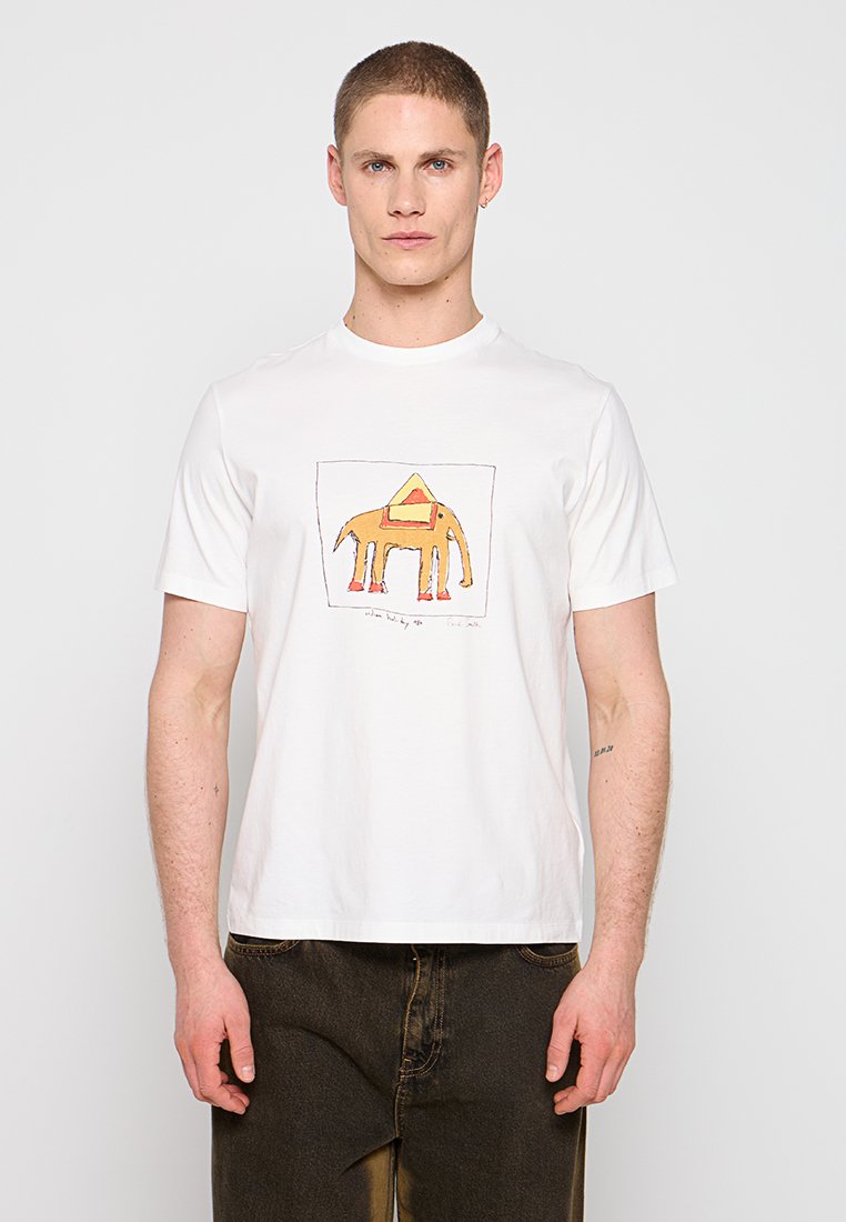 Junger Mann trägt ein weißes T-Shirt mit einem orangefarbenen Elefantengrafik und dunklen Hosen, steht vor einem einfarbigen hellen Hintergrund.