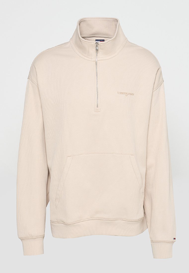 Beiger Pullover mit langen Ärmeln, Halbreißverschluss am Kragen, Kängurutasche, gerippten Bündchen und dezentem "tommyjeans"-Logo auf der linken Brust.