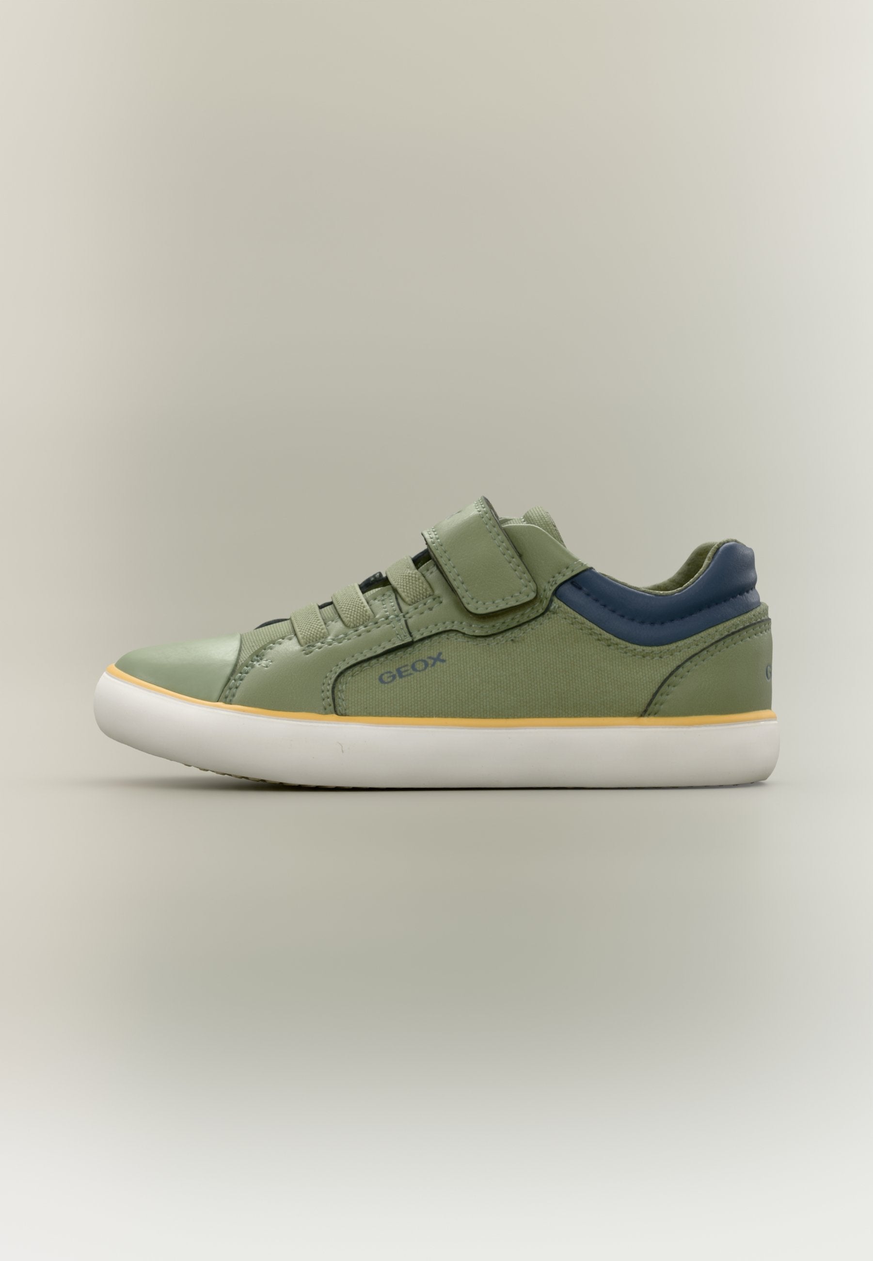Grüner Sneaker in niedrigem Schnitt mit marineblauer Ferse, gelbem Rand, weißer Sohle, Klettverschluss und Schnürsenkeln, Seitenansicht vor neutralem Hintergrund.
