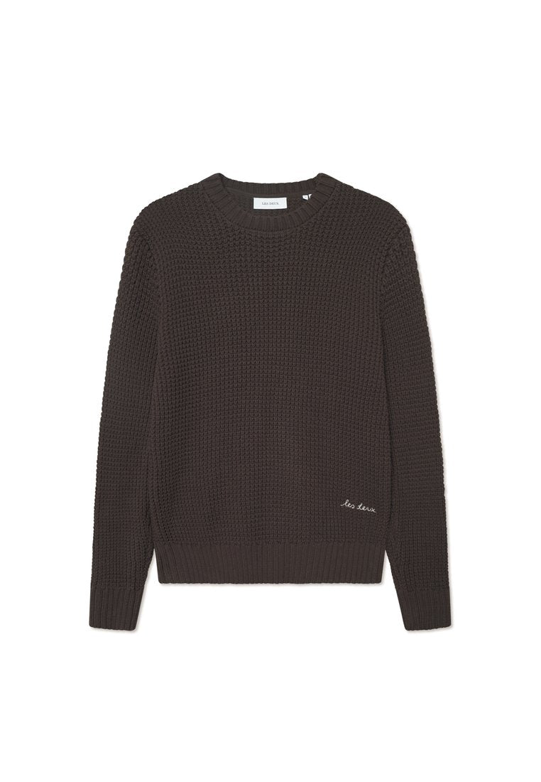 Dunkelbrauner gestrickter Pullover mit rundem Ausschnitt, strukturiertem Muster, gerippten Bündchen und Saum, versehen mit kleinen weißen gestickten Texten am unteren Rand.