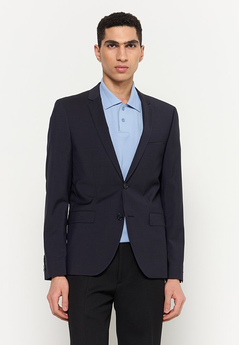 Marineblazer mit zwei Knöpfen, Reverskragen und seitlichen Taschen, getragen über einem hellblauen Poloshirt, kombiniert mit schwarzen Hosen.