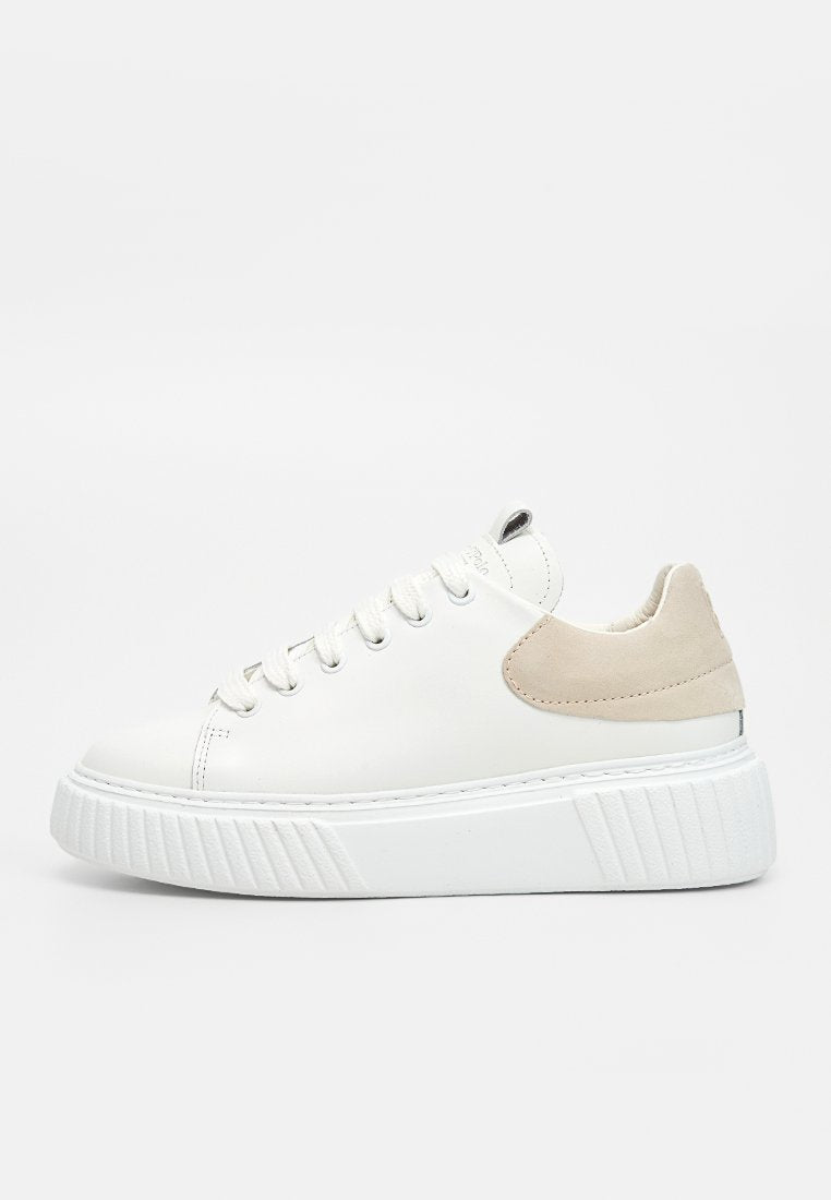 Weißer Sneaker mit niedrigem Schaft, dicker strukturierter Sohle, weißen Schnürsenkeln und beiger Wildleder-Fersenlasche auf einem einfarbig hellen Hintergrund.