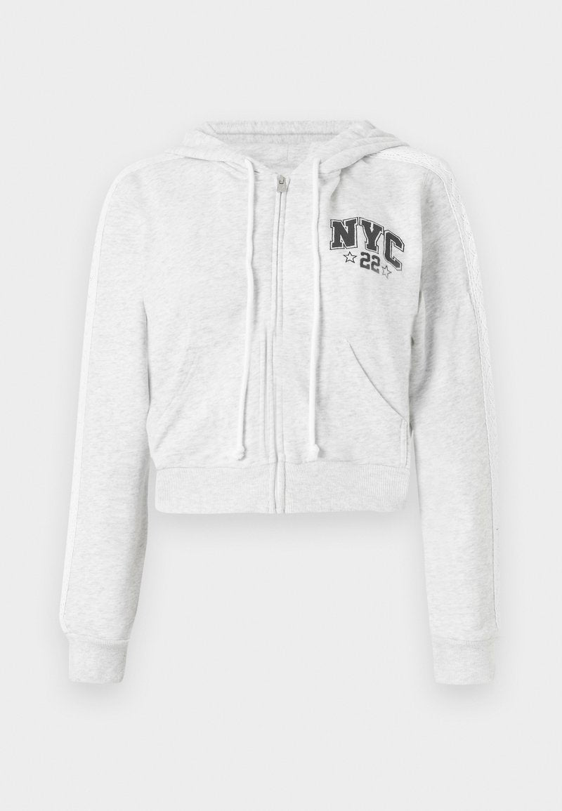 Gekürzter grauer Hoodie mit Frontreißverschluss, Kordelzug, NYC-Grafik und gerippten Bündchen. Weicher Stoff mit glatter Textur und kontrastierenden Seitenstreifen.