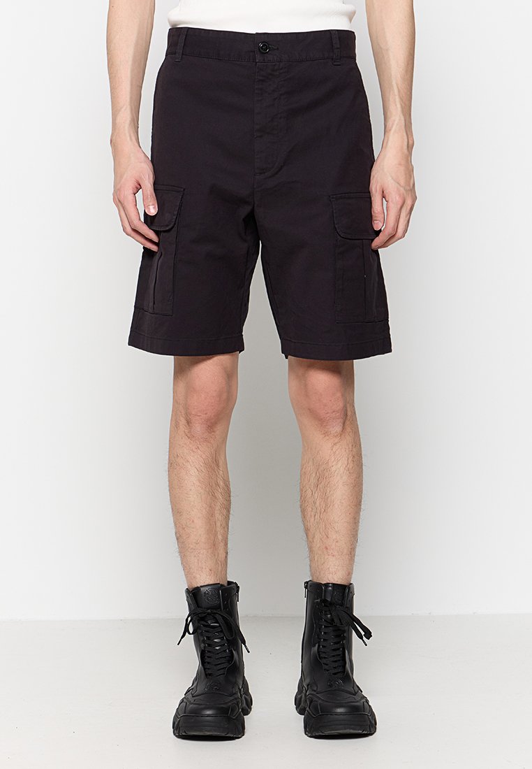 Schwarze Cargo-Shorts aus Baumwolle, mit zwei seitlichen Taschen, einem Knopfverschluss und einem knielangen Schnitt. Getragen mit schwarzen Schnürstiefeln.
