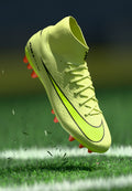 Gelbe Fußballschuhe mit schwarzen Akzenten, hohem Knöchelkragen und pinken Stollen. Strukturiertes Material, leichtes Design, erhöht über dem Gras.