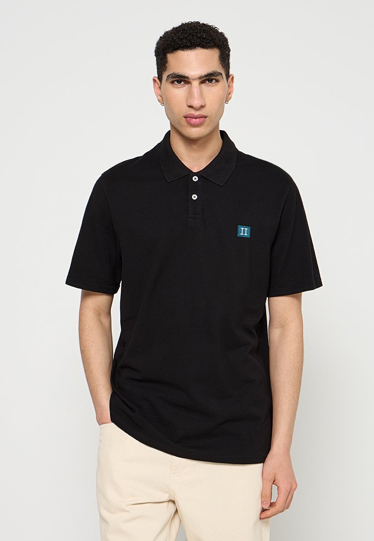 Schwarzes Poloshirt aus Baumwolle mit Kragen, kurzen Ärmeln und zwei weißen Knöpfen. Es hat ein kleines blaues Logo auf der Brust.