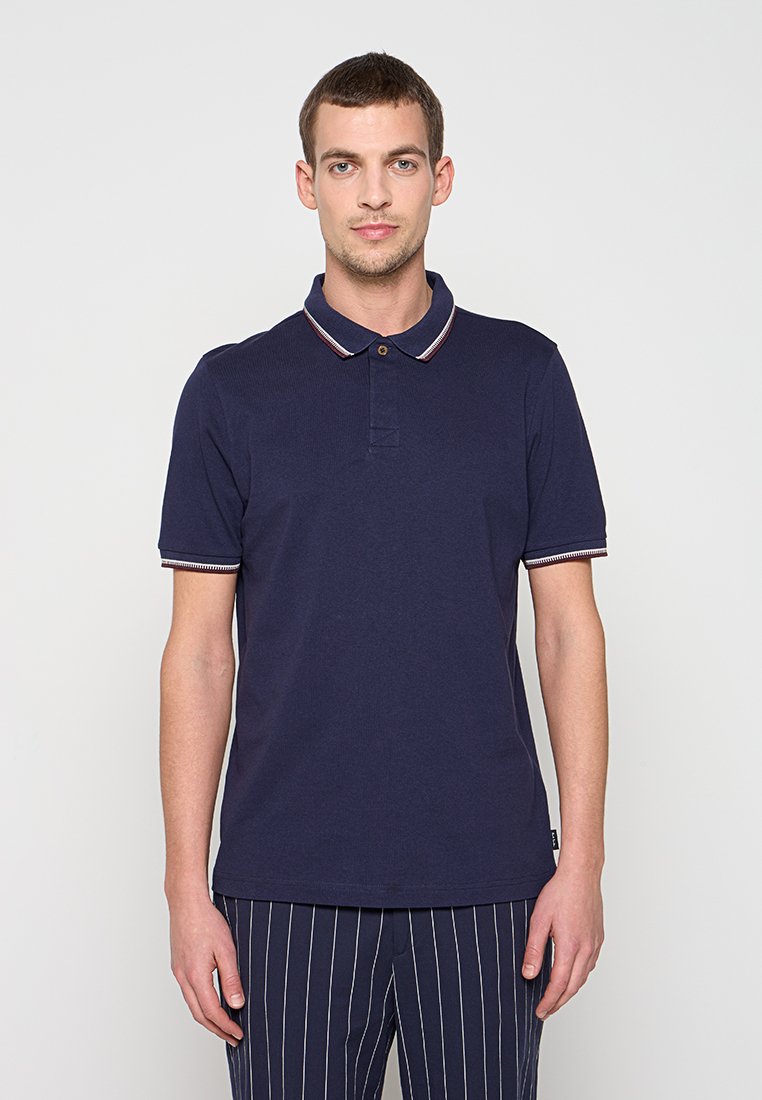 Marineblaues Poloshirt mit Kragen und kontrastierenden hellen Streifen. Der Stoff wirkt strukturiert, und das Design umfasst eine Knopfleiste.